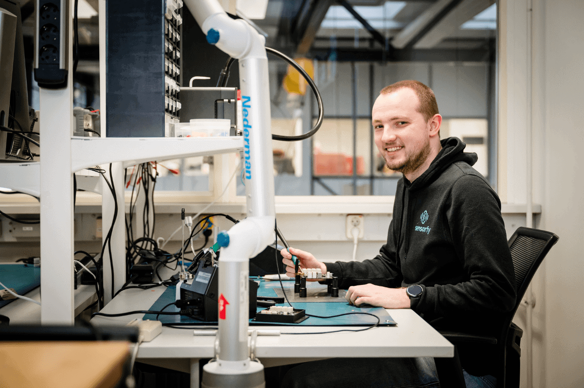 Elektronica-werkplek in lab Persoon aan een werkbank met gereedschap; apparatuur zichtbaar.